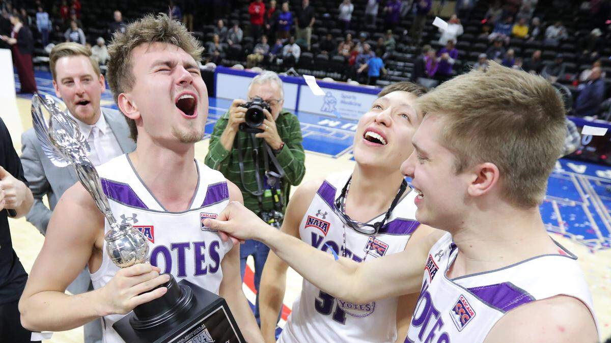 College of Idaho’s Connor Cooper celebrates with the NAIA national championship trophy with Yotes teammates Bryan St. Clair, middle, and Whitt Miller at Municipal Auditorium Saturday night. The Yotes held off a comeback attempt by Indiana Tech to win their second national title, 73-71.