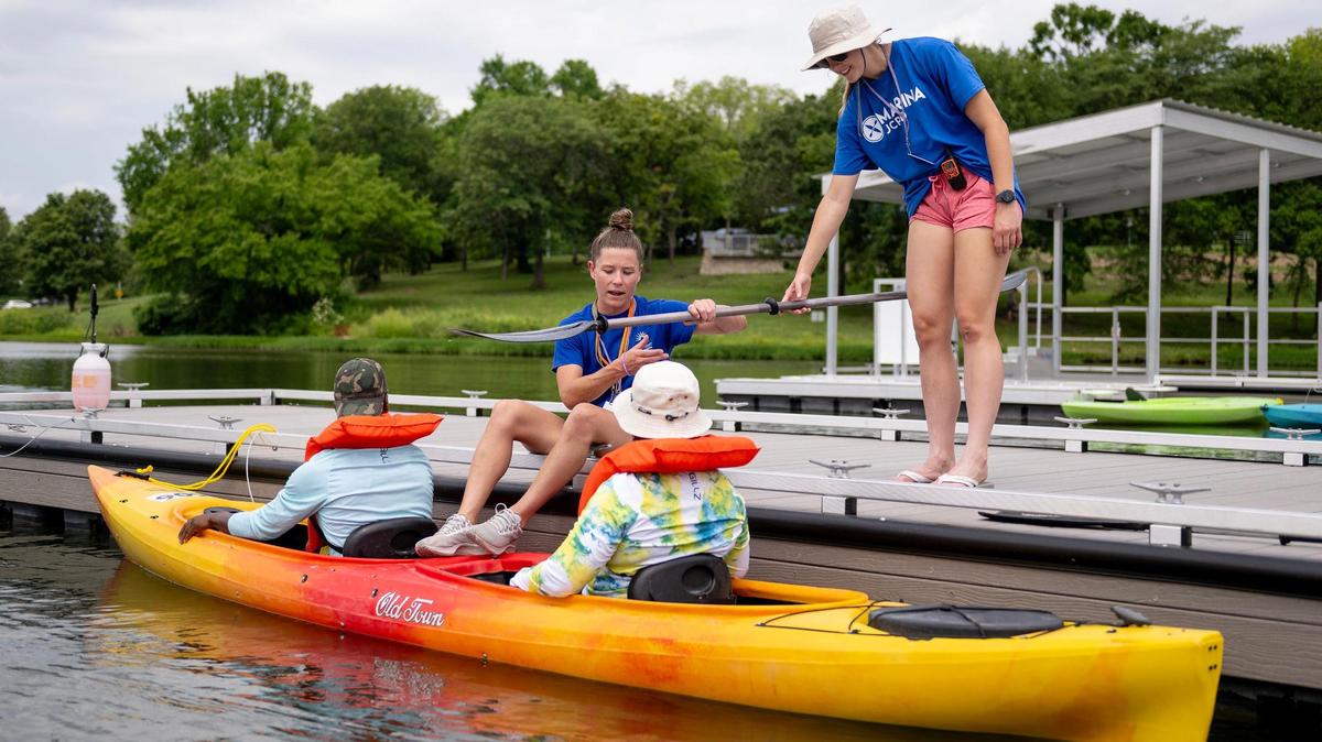 Paige Herrmann, left, an aquatics coordinator for the Johnson County Park and Recreation District, and Mia Klopfenstine, a lifeguard, helps boaters with a paddle at the newly-renovated marina at Shawnee Mission Park on Wednesday, July 12, 2023, in Shawnee, Kan.