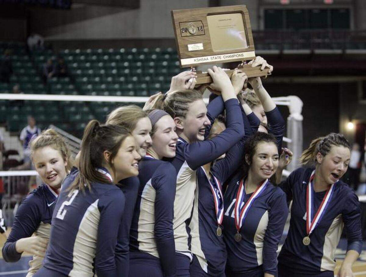 The St. Thomas girls volleyball team celebrates with their medals at trophy after defeating St. James to take first place in the 2014 5A KSHSAA State Volleyball Championships Saturday afternoon at the Kansas Expocentre.