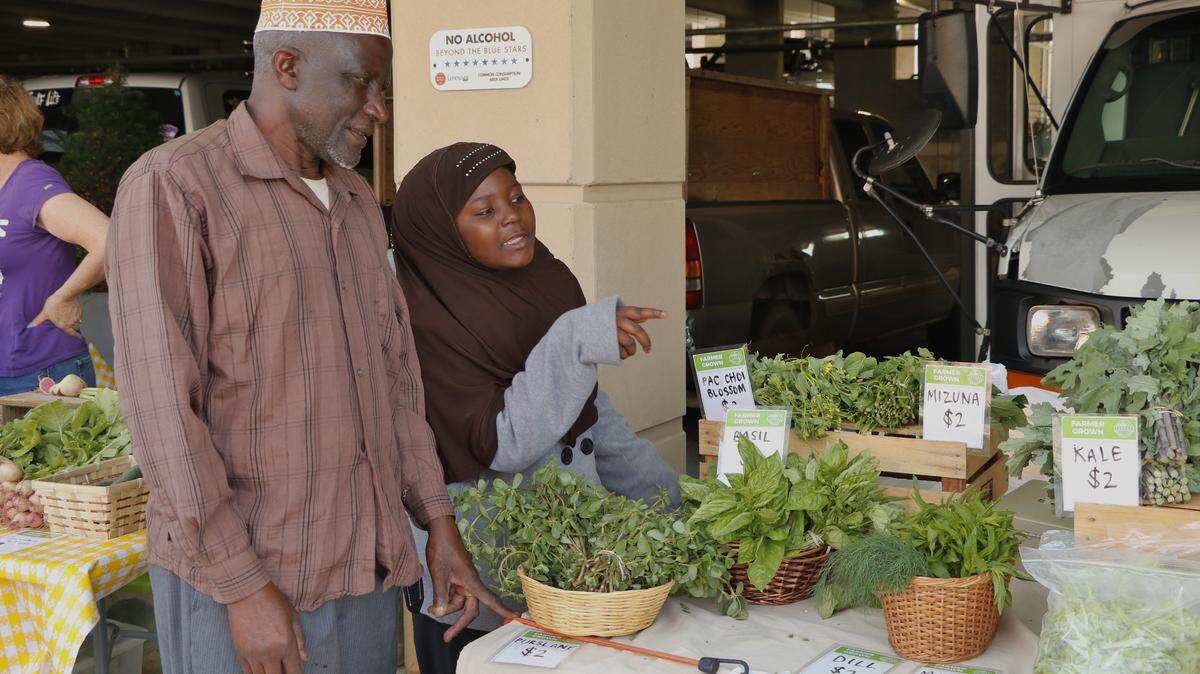 During a 2023 Lenexa Farmers Market, refugees Ibrahim Dugudu and his daughter, Amina Ibrahim, 10, discussed the produce they had grown and were selling at the market. Dugudu is in his second year of the four-year Roots for Refugees program.
