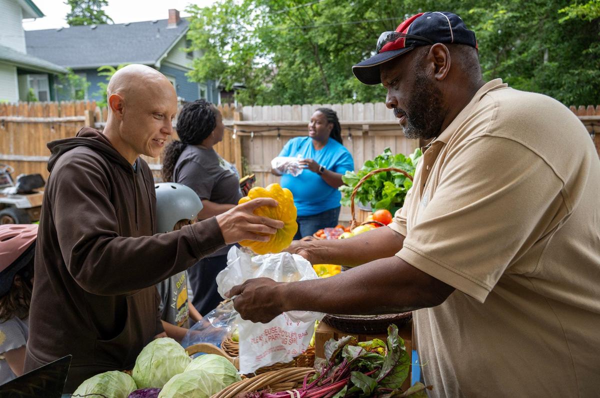 Local patron, Brice Young, left, drops a squash into a bag while buying produce from farm owner, Alan Young, right, at The Young Family farm in Kansas City.