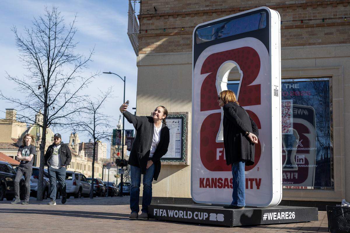 People take photos next to a FIFA World Cup 26 sign that stands on the corner of Pennsylvania Avenue and Nichols Road at the Country Club Plaza on Tuesday, Dec. 16, 2025, in Kansas City.