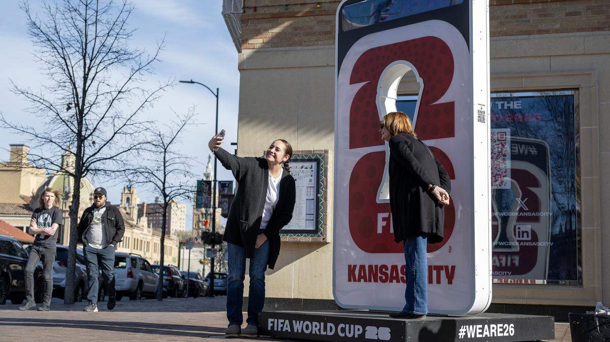 People take photos next to a FIFA World Cup 26 sign that stands on the corner of Pennsylvania Avenue and Nichols Road at the Country Club Plaza on Tuesday, Dec. 16, 2025, in Kansas City.