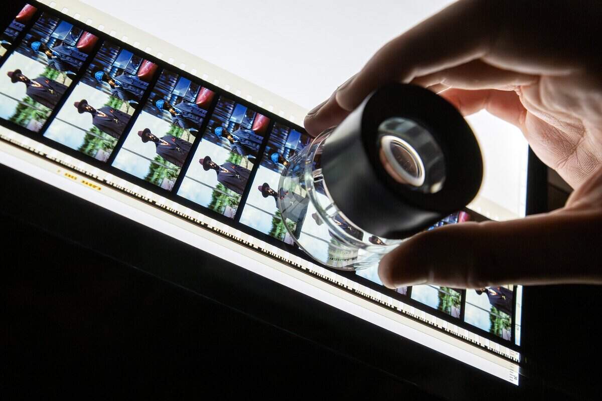 Projectionist Ethan Foster uses a magnifying glass to inspect a frame from a 70mm film reel under a light while threading it during a screening of “Sinners” at Screenland Armour Theatre on Friday, March 27, 2026, in North Kansas City.