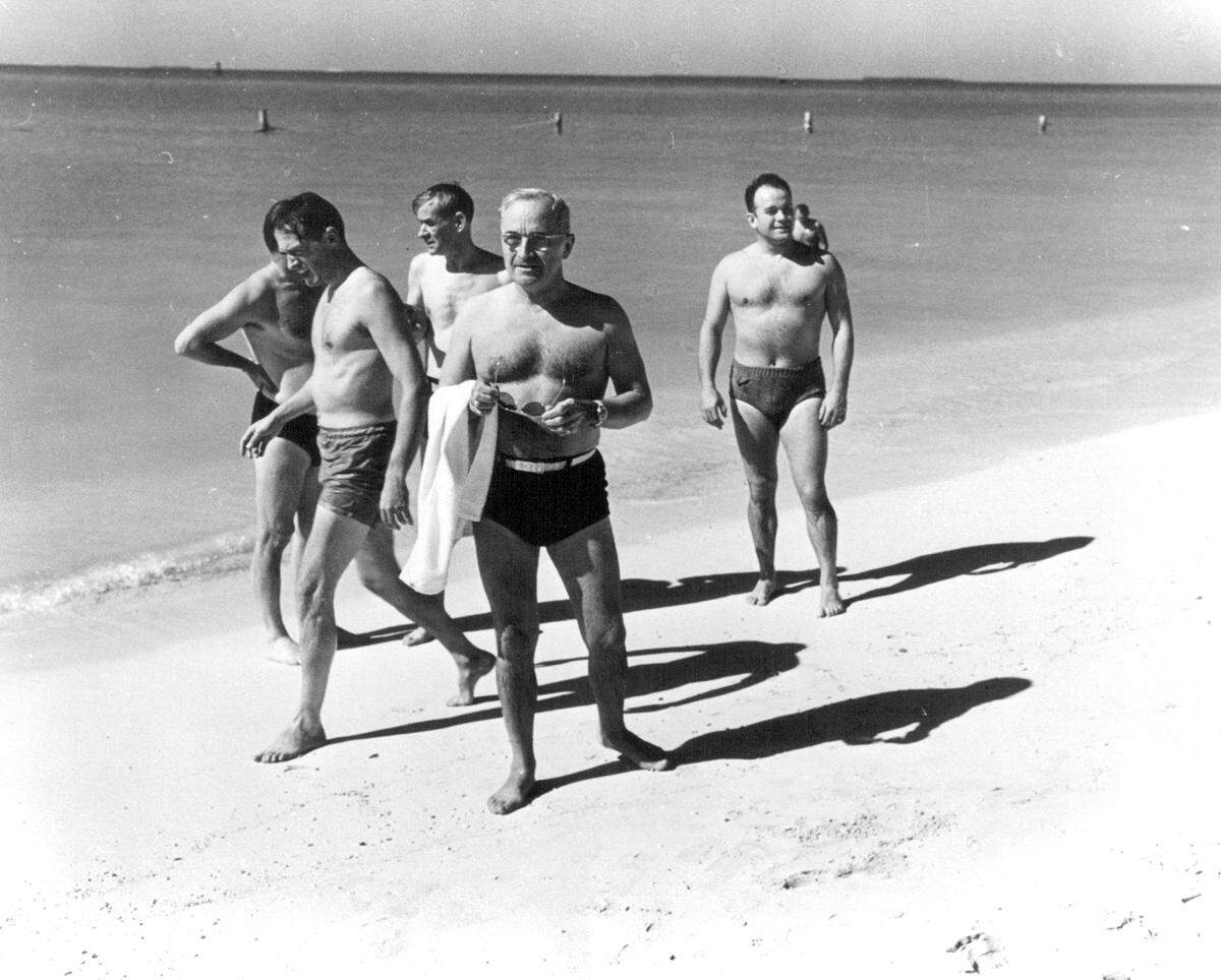 President Harry S. Truman appears in swimming trunks on a beach, surrounded by unidentified people, in an undated photo.