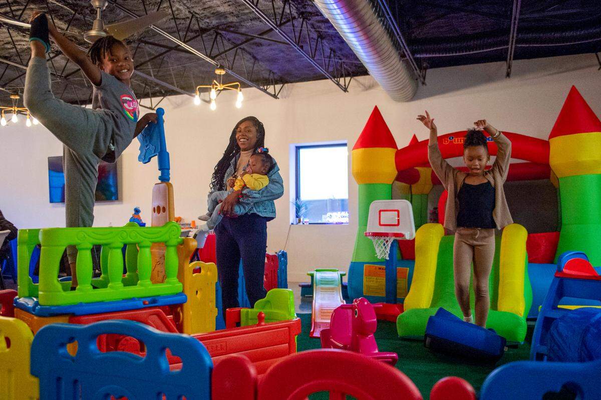 Diamond Fuse holds 8-month-old Rylie Luster, while older sister Qumora Griffin, 8, left, and 7-year-old cousin Liberty Wilson enjoy the birthday party play area.