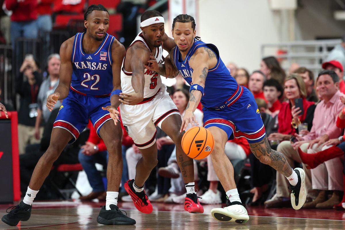 Tre Holloman #5 of the NC State Wolfpack defends Tre White #3 of the Kansas Jayhawks while Darryn Peterson #22 looks on at Lenovo Center on December 13, 2025 in Raleigh, North Carolina.