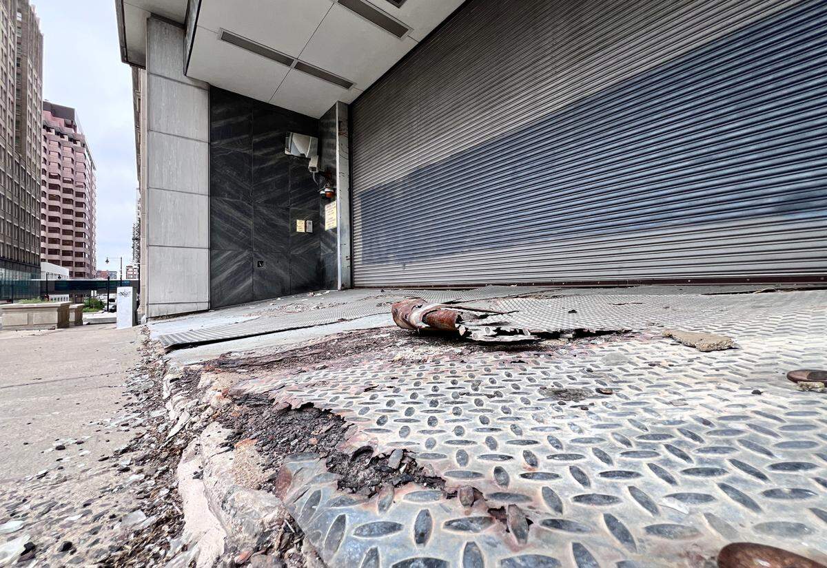 Crumbling concrete and broken pavement surround the entrance to the former Federal Reserve building’s parking area at 925 Grand, a stark sign of years of neglect.
