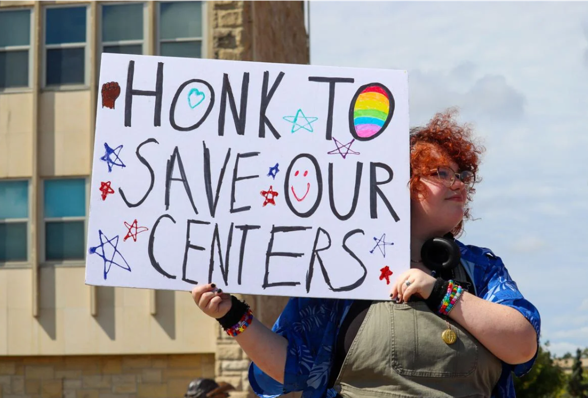 Travis Meredith holds up a protest sign reading “HONK TO SAVE OUR CENTERS” at the Save Our Centers KU rally on Tuesday, Sept. 17, 2024.
