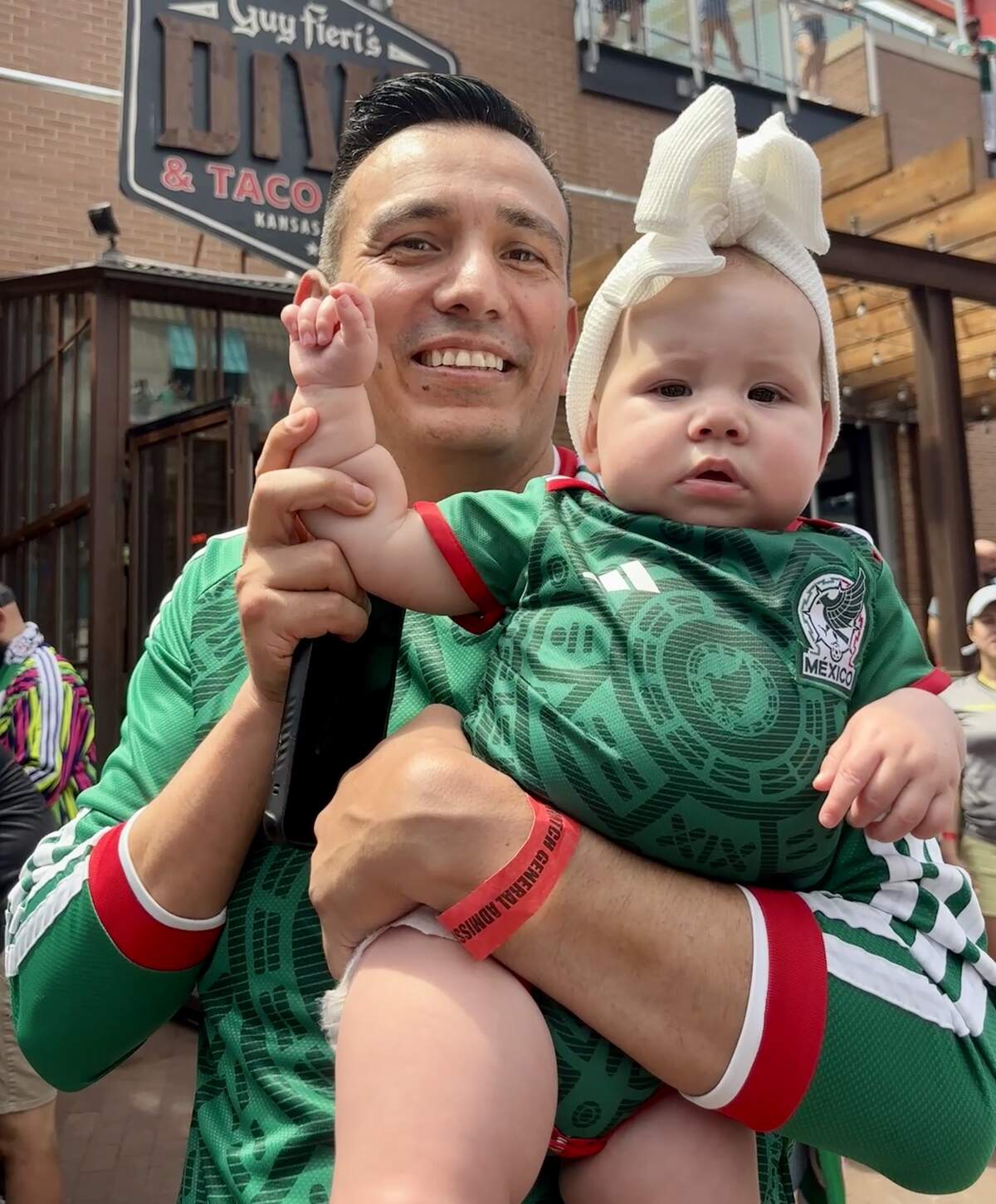 Jesus Ramirez poses with 7-month-old Gwendolyn Ramirez at the Power and Light District. The pair wore Mexico jerseys to the watch party for the opening match of the 2026 FIFA World Cup. June 11, 2026.