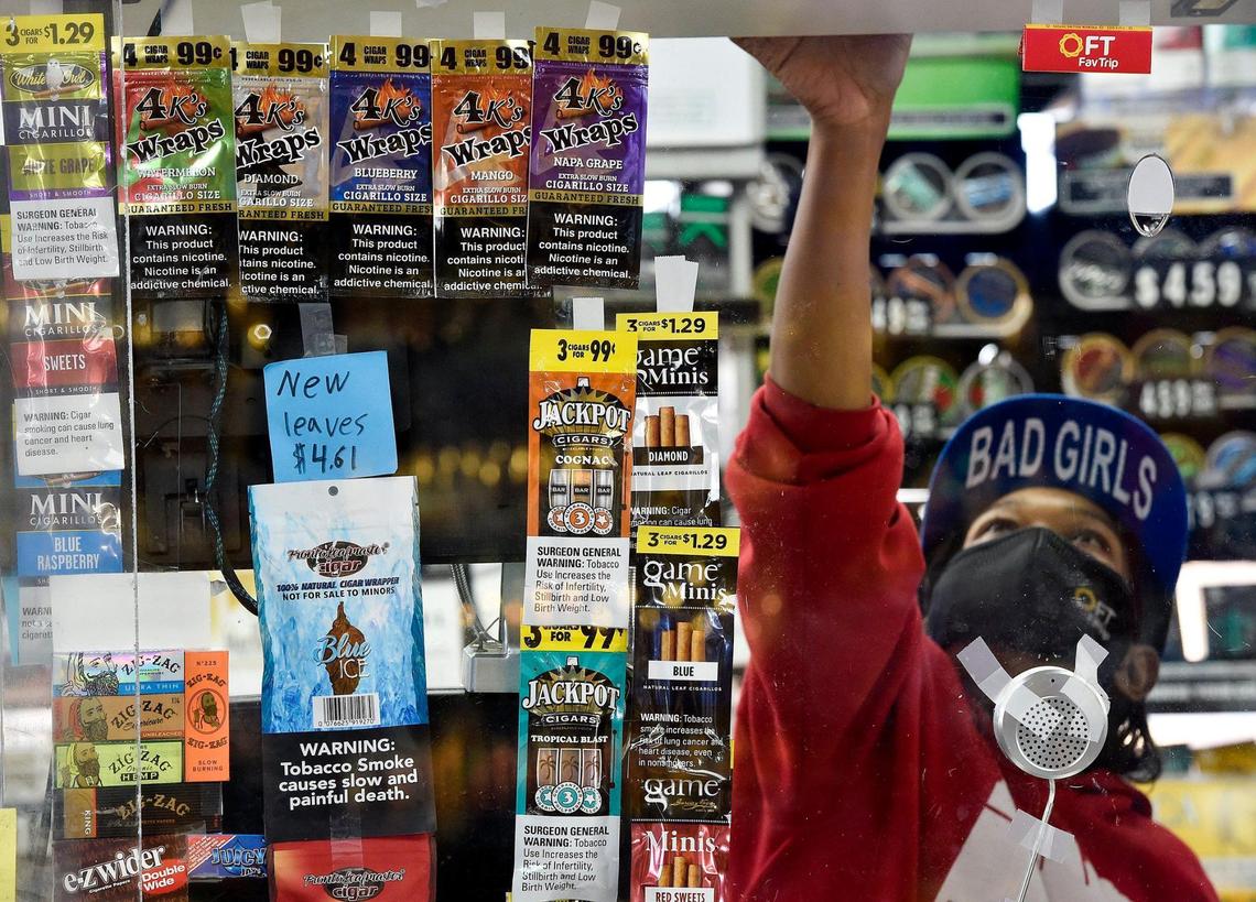 Behind flavored tobacco products taped to the window, Cindy Lewis, a cashier at the south Kansas City convenience store Fav Trip, gets a flavored tobacco product for a customer. An effort to ban these products failed a City Council committee vote.