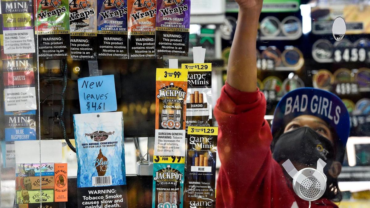 Behind flavored tobacco products taped to the window, Cindy Lewis, a cashier at the south Kansas City convenience store Fav Trip, gets a flavored tobacco product for a customer.