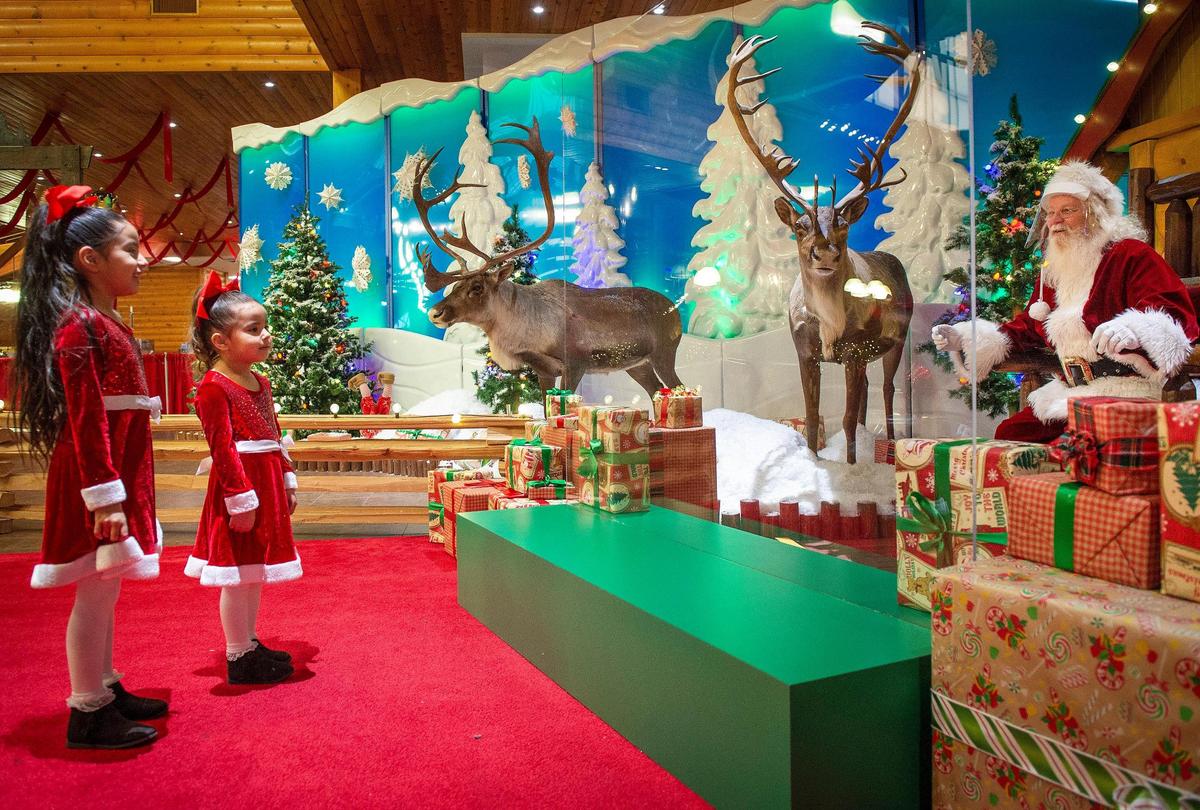 Jacquie Sandiego, 6, left, and her sister, Dalary Sandiego, 4, of Wyandotte County, talked to Santa, also known as Ricky Kell, who sat behind a plexiglass shield at Cabela’s on Wednesday, Dec. 2, 2020, in Kansas City, Kansas. Cabela’s is taking reservations to visit Santa and is operating with COVID-19 precautions in place. The visits with Santa include temperature checks, masks, and sanitizing after each guest.