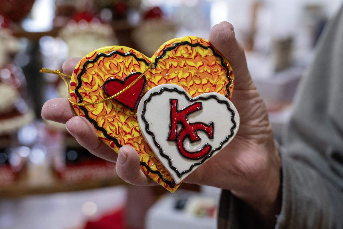 Fernando Bozzoli displays a heart-themed Kansas City Chiefs ceramic ornament made by his wife, ceramic artist Irma Starr, as she gives a tour of her home studio on Thursday, Dec. 11, 2025, in Kansas City.