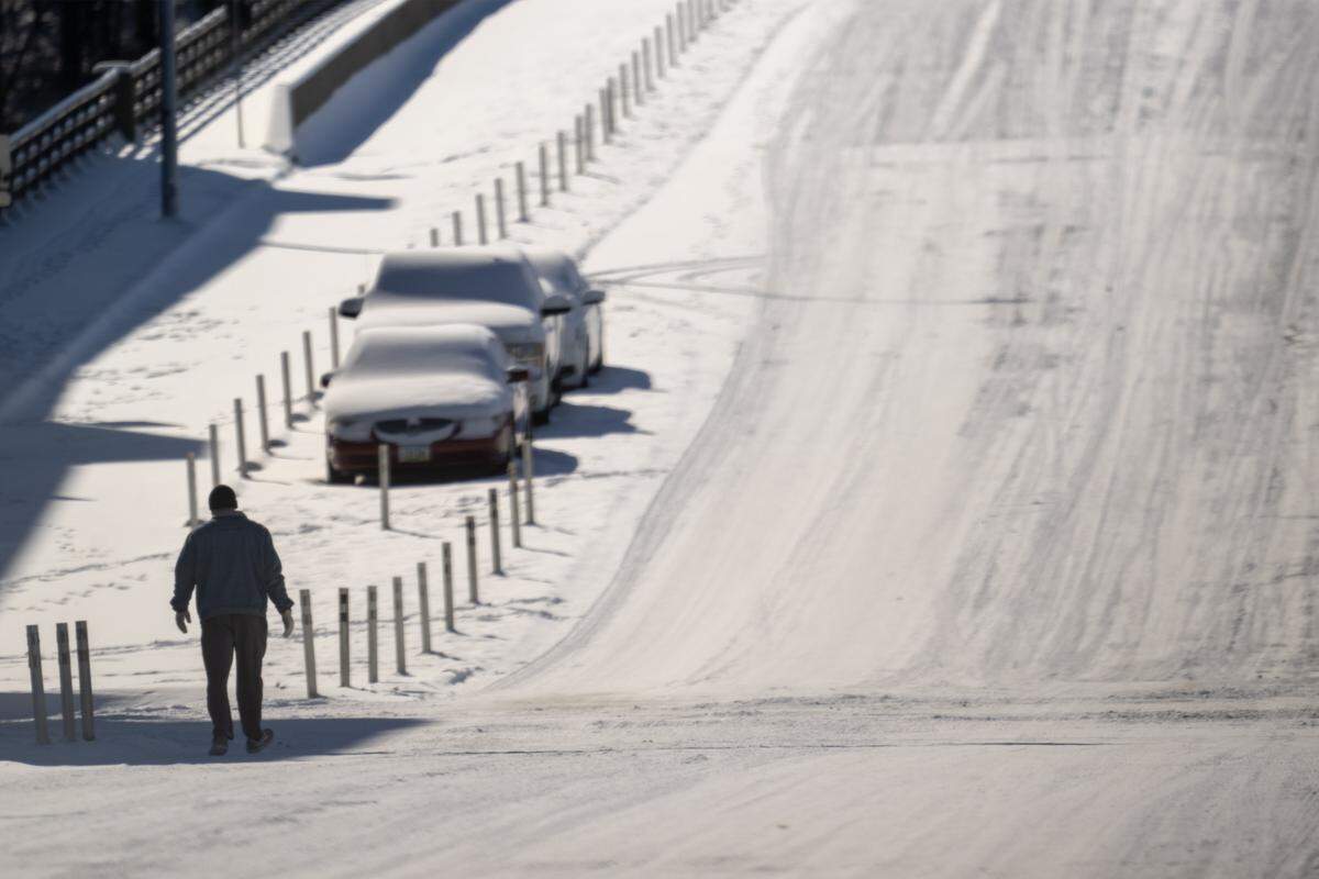 A pedestrian navigates the slick, snow-covered pavement of McGee Street on Sunday, Jan. 25, 2026, following a weekend storm that left Kansas City buried and shivering in bitterly cold temperatures