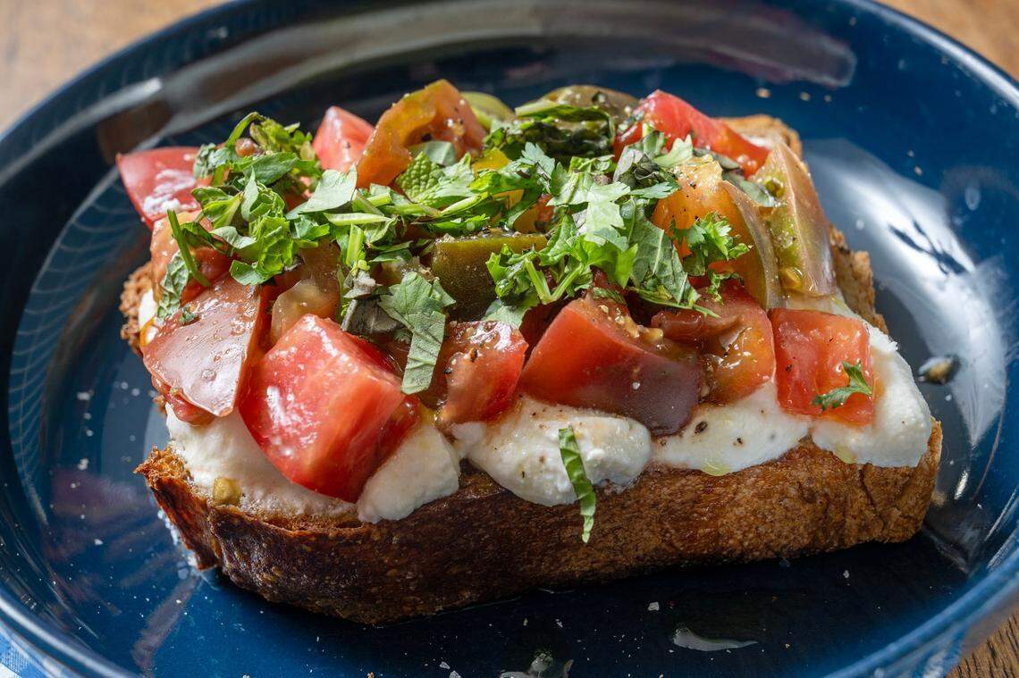 Heirloom Tomato Toast featuring Ibis country bread, heirloom tomatoes, ricotta, herbs, olive oil available for $9 At Hemma Hemma, 7122 Wornall Rd, Kansas City.