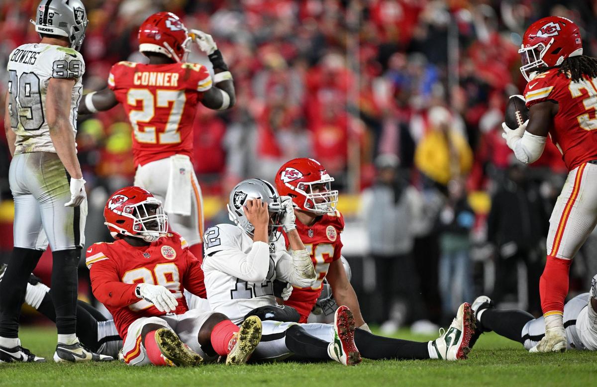 Las Vegas Raiders quarterback Aidan O’Connell (12) held his head in his hands while Kansas City Chiefs defensive tackle Tershawn Wharton (98) and defensive end George Karlaftis (56) watched the replay of a botched snap that resulted in a fumble ending the Raiders’ chance of winning the game on Friday, Nov. 29, 2024, at GEHA Field at Arrowhead Stadium. Kansas City Chiefs linebacker Nick Bolton (32), right, recovered the fumble.