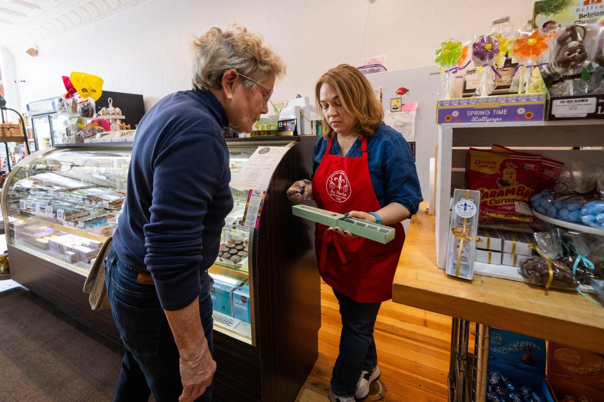Lora Wiley, owner of Au Marché, helps a customer fill a chocolate box in Lawrence on Wednesday, April 9, 2025. Wiley anticipates needing to absorb some of the additional costs of doing business related to the Trump administration’s tariff policy on European imports.