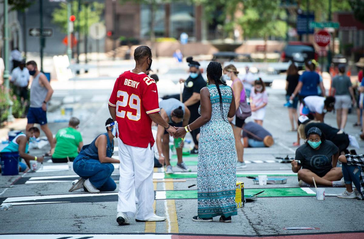 Two volunteers held hands after they took a break from painting to dance with each other at the Black Lives Matter mural being painted on 10th St. Saturday between Wyandotte and Baltimore.