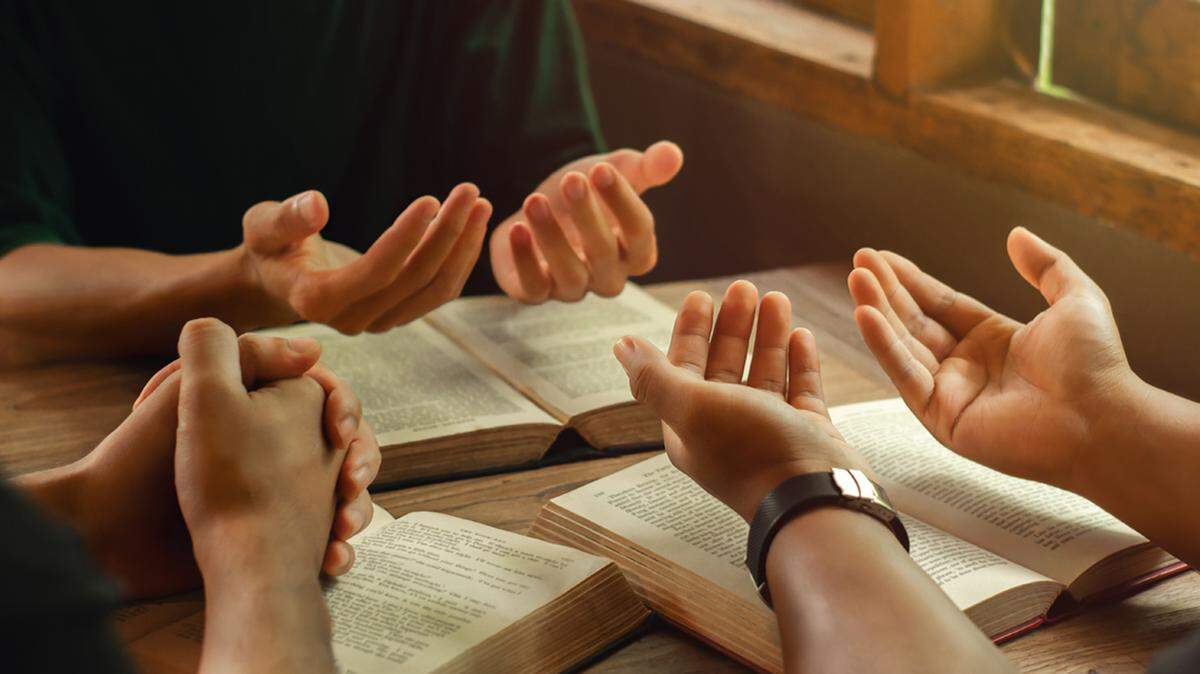 A group of young people holding hands in prayer.