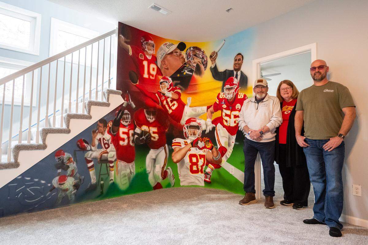 Homeowners Ed and Mary Ellen Hughes, left, and Kansas City artist Craig Greco stand next to a mural of past and present Kansas City Chiefs eras that Greco painted in their Liberty home after the house almost burned down last year.
