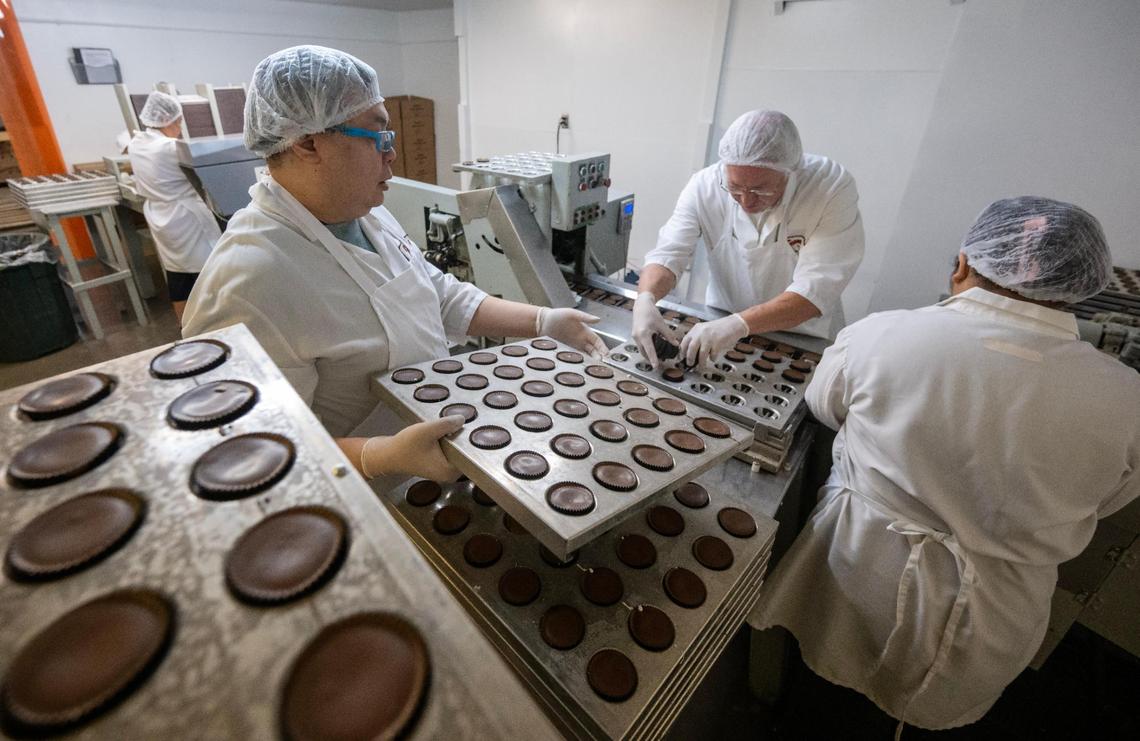 Bob Khotbounheuang, from left, brings a full tray of Valomilks as Dave Swiercinsky, left, and Tana Vongchantha, place the marshmallow-filled cups onto a conveyor belt for packaging during a production run at the Merriam plant.