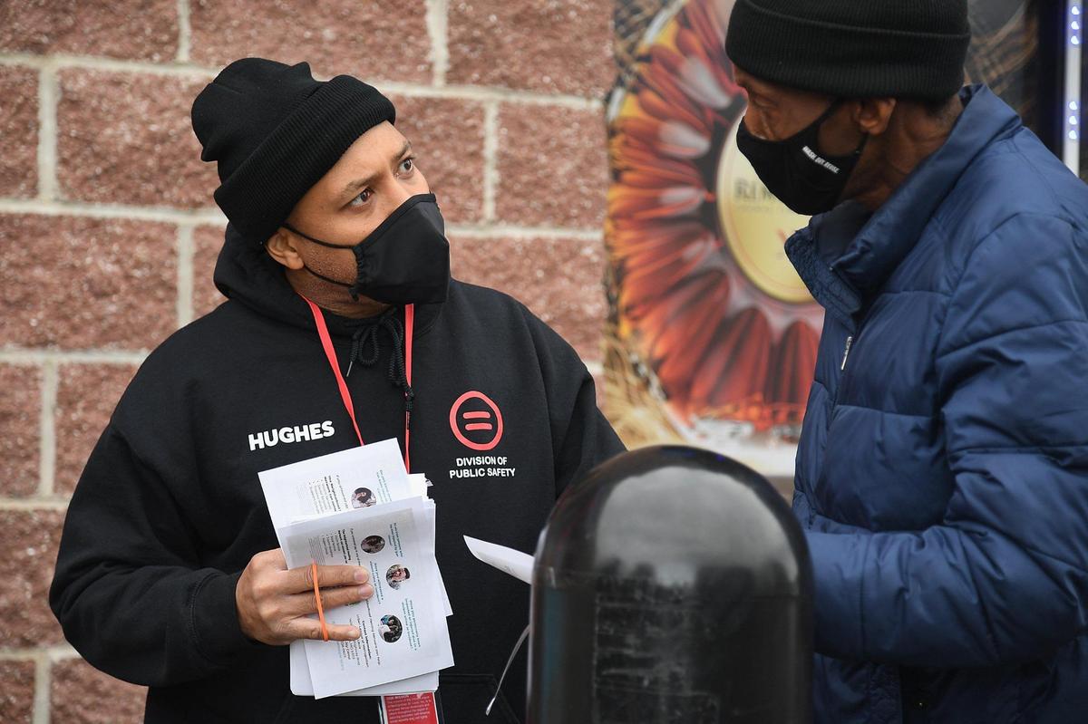 Sean Hughes provides pamphlets on services to a visitor during a “Serving Our Streets” event in St. Louis. One team with the SOS initiative de-escalated 89 conflicts in 2021, according to program leaders.