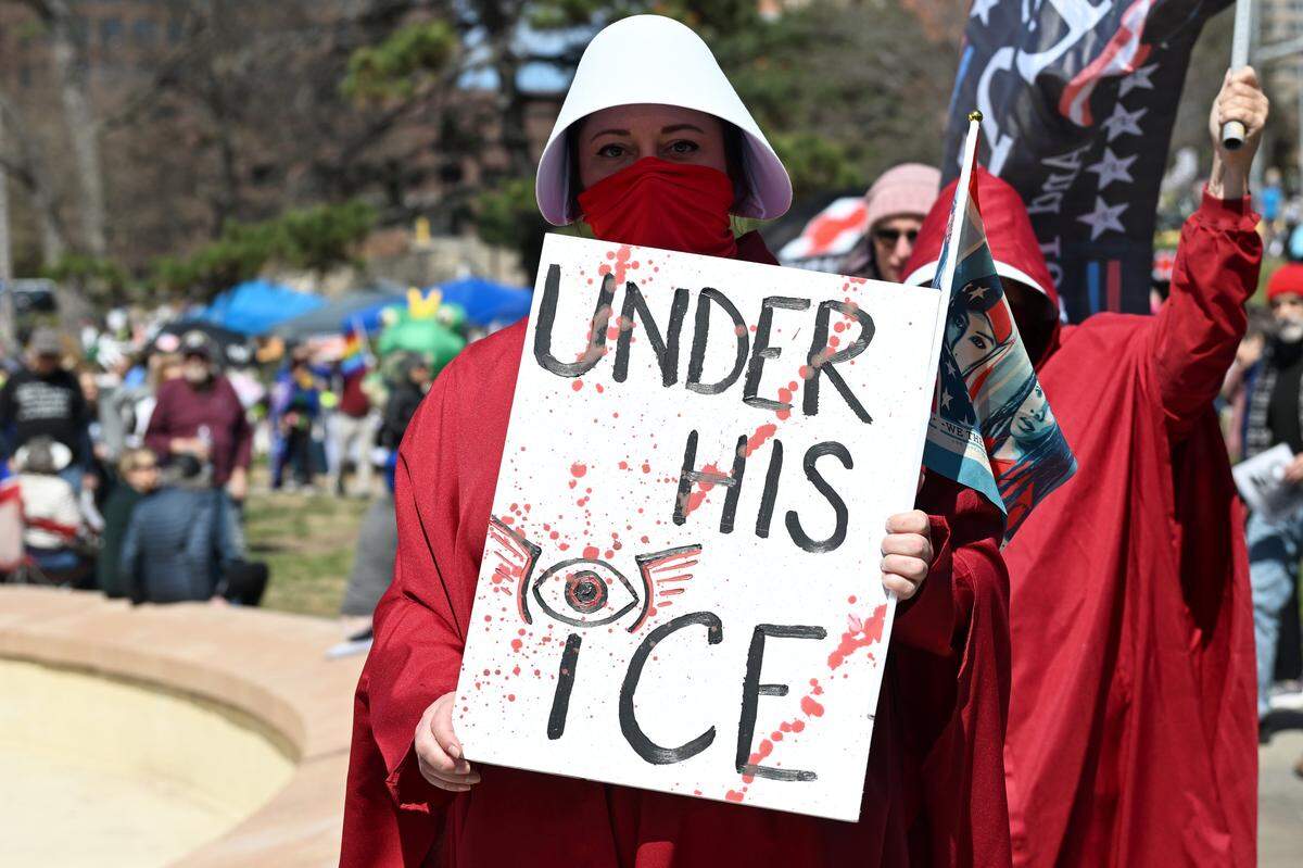 A protester dressed as a character from “The Handmaid's Tale” holds a sign during a No Kings protest at Mill Creek Park near the Country Club Plaza on Saturday, March 28, 2026, in Kansas City.