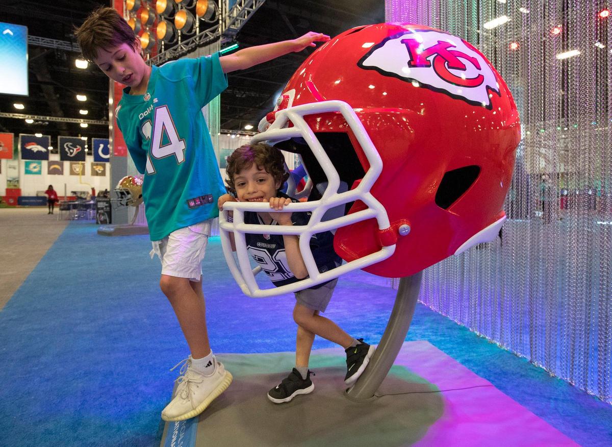 Mico Estrella, 10, and Franco Estrella, 4, of Miami play around a large Kansas City Chiefs helmet on display Saturday during the Super Bowl Experience at the Miami Beach Convention Center.