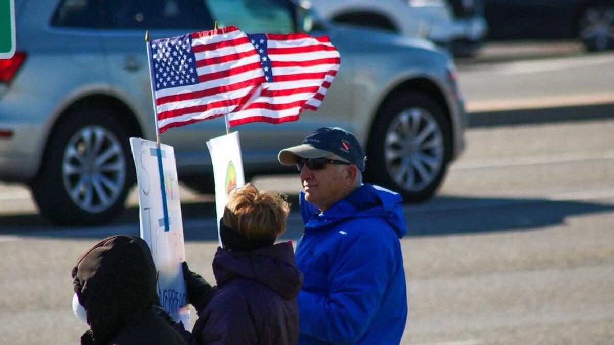Jim Twigg, 68, holds signs with American flags attached to them at the No Kings rally at 119th Street and Metcalf Ave in Overland Park on March 28, 2026.