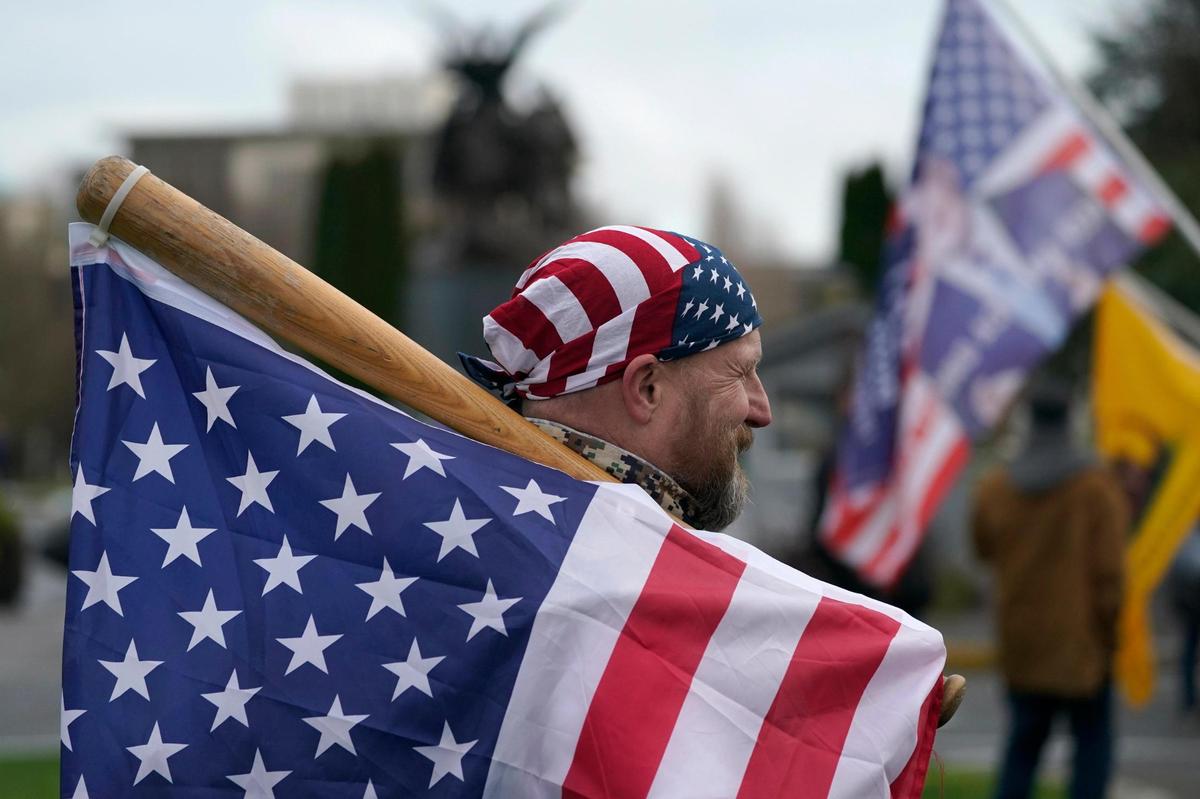 A man carries a U.S. flag attached to a baseball bat as he waits at the Capitol in Olympia, Wash., Wednesday, Jan. 6, 2021, before the start of a protest rally against the counting of electoral votes in Washington, DC, affirming President-elect Joe Biden’s victory. People supporting President Donald Trump and other supporters began arriving at the Capitol mid-morning for a protest rally Wednesday that was expected to begin at noon. (AP Photo/Ted S. Warren)