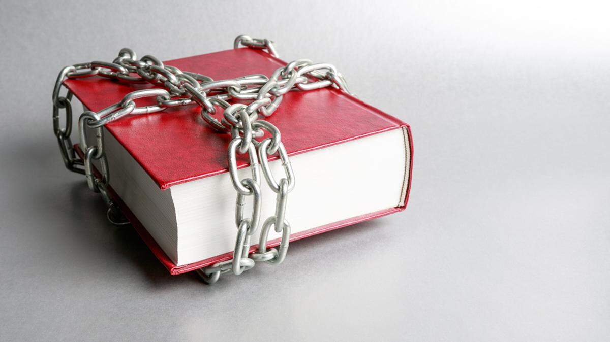 book ban banned illustration censor censorship objection library school parent remove on a gray background is a red book wrapped around a metal chain