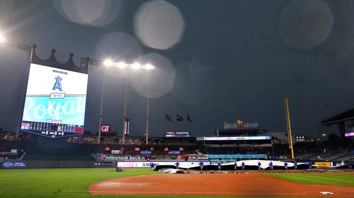 Kansas City Royals grounds crew members drag a tarp onto the field during a rain delay in the game against the Los Angeles Angels at Kauffman Stadium on April 26, 2026 in Kansas City, Missouri.