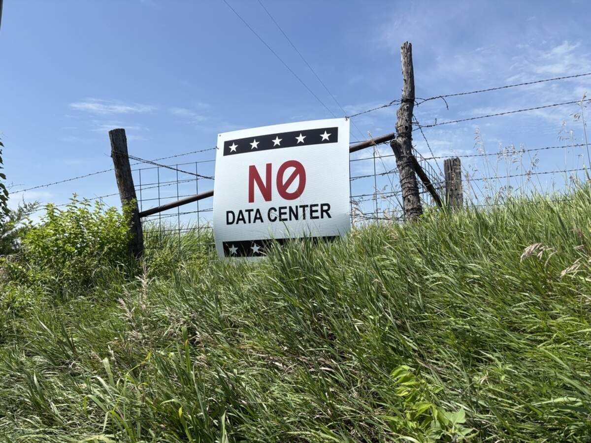 A white, blue and red sign hangs on a fence and reads “NO data center.”