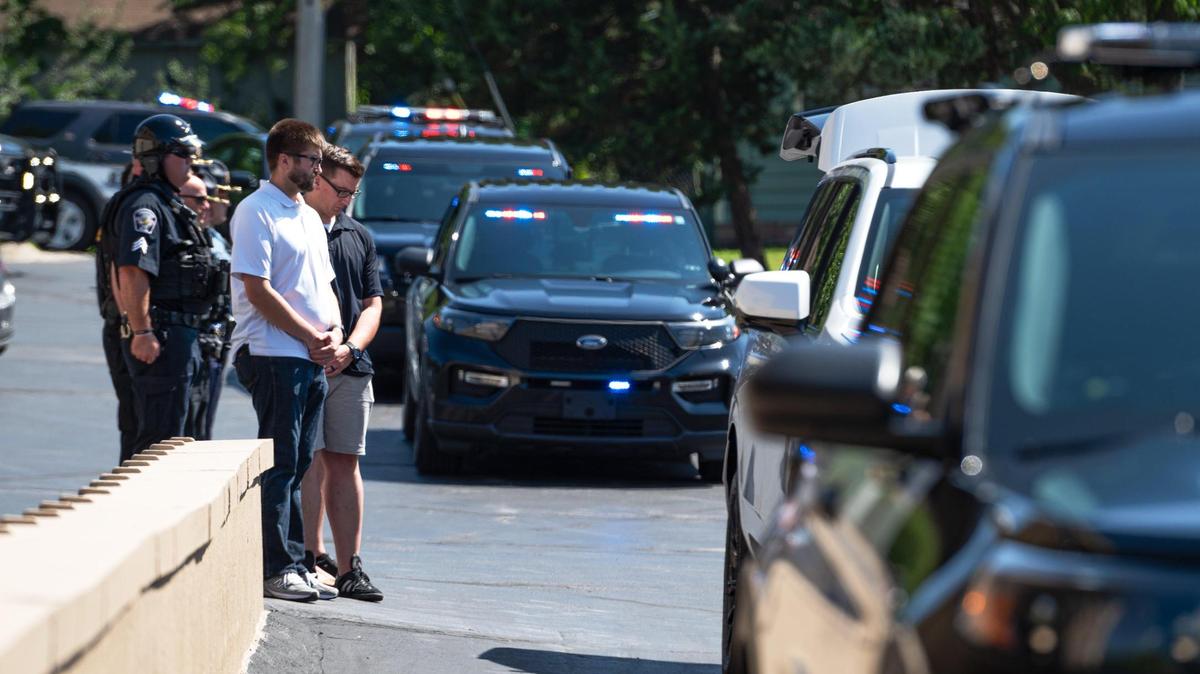Mourners bow their heads Tuesday, Aug. 8, 2023, as the remains of Officer Jonah Oswald are moved into the Amos Family Funeral Home and Crematory in Shawnee. Oswald was killed after a shooting unfolded inside of a QuikTrip on Sunday, Aug. 6, 2023, in Mission.