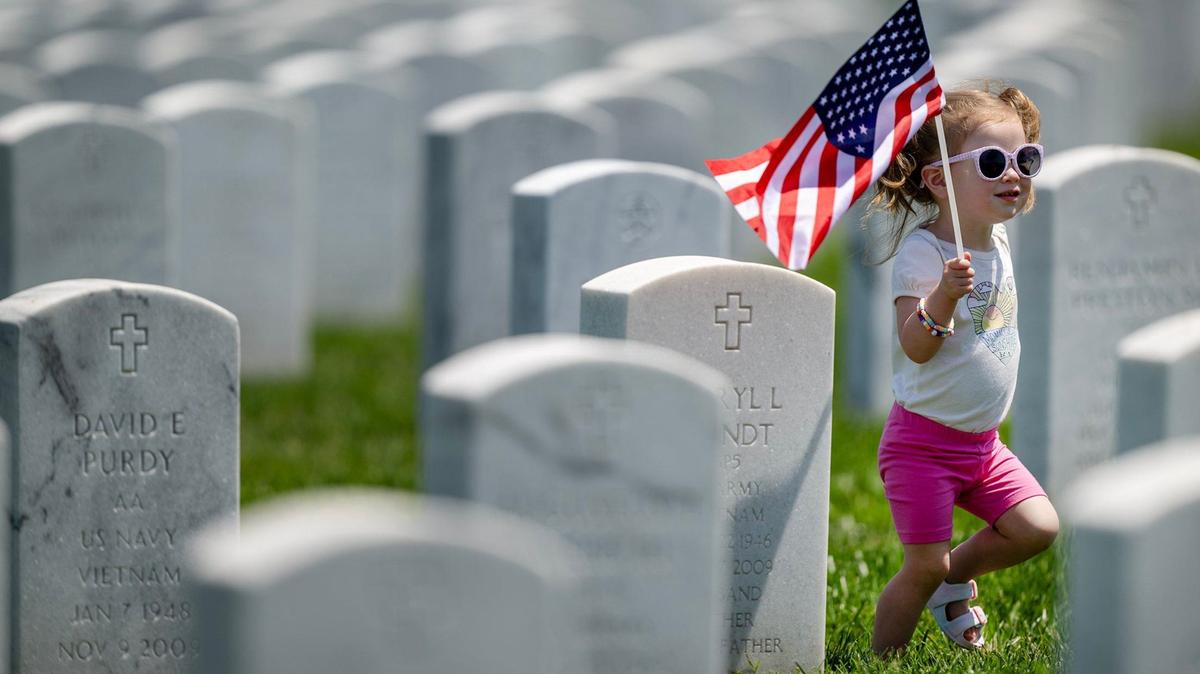 Eva Montis, 2, of Kansas City, carries an American flag during an outing to visit the grave of her grandfather, Gerald Johnson, an Air Force veteran who served in Vietnam and is buried at Leavenworth National Cemetery, on Thursday, May 23, 2024, ahead of the Memorial Day holiday. Eva was with her mother, Kara Montis and grandmother, Brenda Johnson.