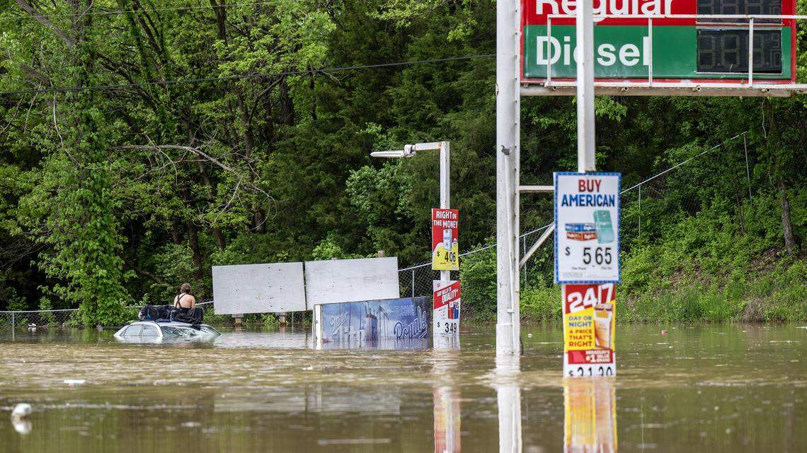 A person sits on top of a vehicle surrounded by flooding waters near the Fisca gas station at the corner of Old 23 Street and Television Place on Monday, April 27, 2026, in Kansas City.