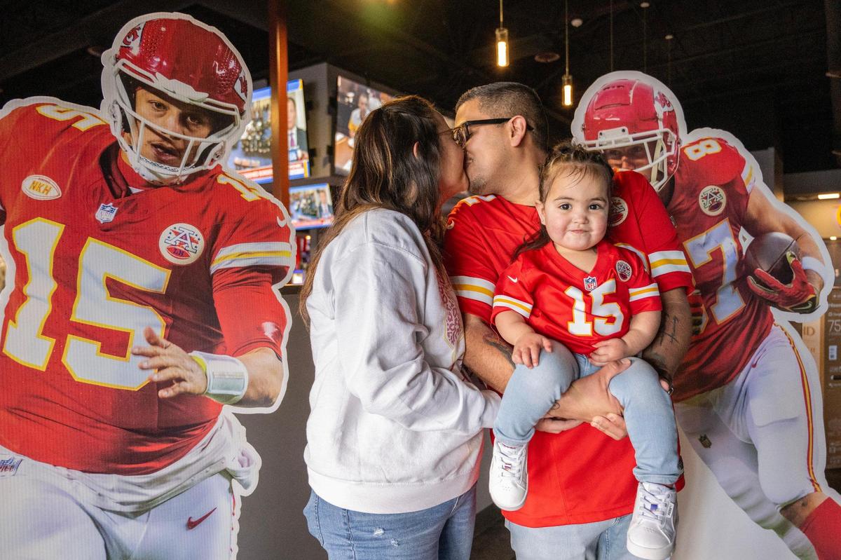 Jazmine Romero, left, and her husband Samuel, both Kansas City Chiefs fans, share a kiss while holding their two-year-old daughter Elise as they pose with life-size cutouts of Kansas City Chiefs quarterback Patrick Mahomes and tight end Travis Kelce on Wednesday, Feb. 7, 2024, in Albuquerque, N.M.