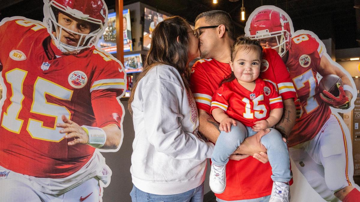 Jazmine Romero, left, and her husband Samuel, both Kansas City Chiefs fans, share a kiss while holding their two-year-old daughter Elise as they pose with life-size cutouts of Kansas City Chiefs quarterback Patrick Mahomes and tight end Travis Kelce on Wednesday, Feb. 7, 2024, in Albuquerque, New Mexico.