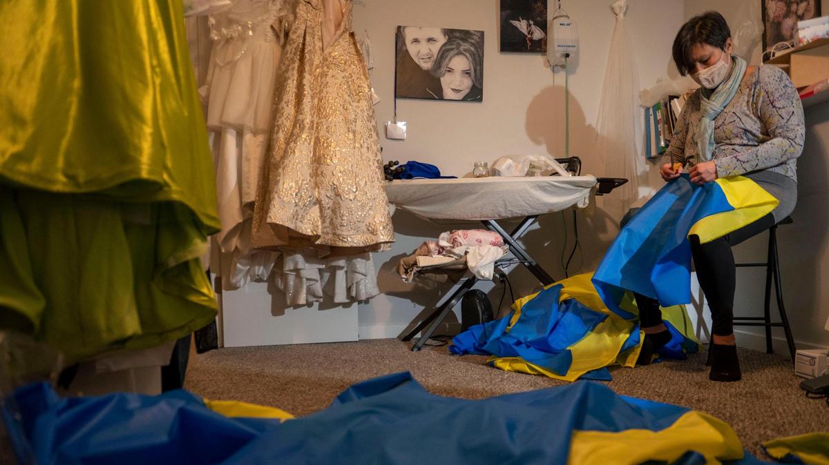 Aiman Dvorak cuts excess thread from freshly made Ukrainian flags at Olga Potapenko’s home in Independence on Thursday, March 3, 2022. Potapenko is a wedding dress designer who has opened her home to help create Ukrainian flags as a thank you to anyone who has donated to support Ukraine.