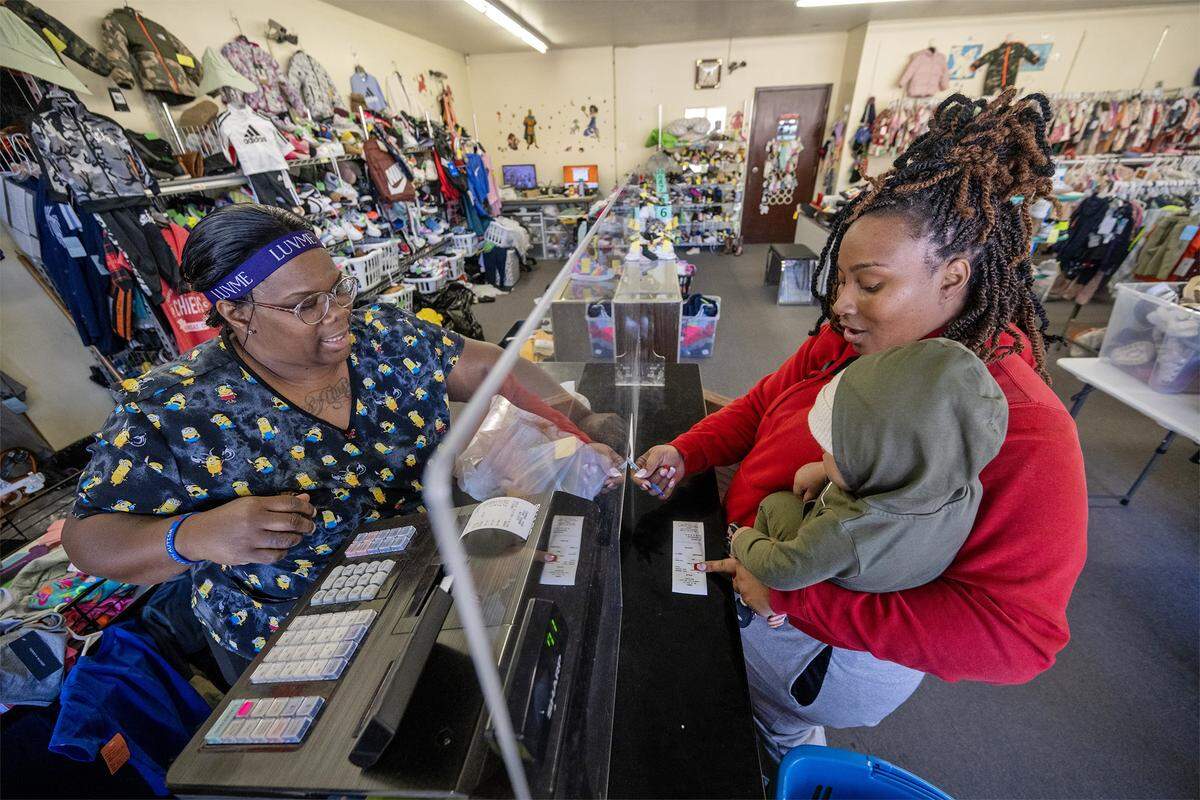 Employee Shawntae Simmons, rings up items for Janeisha Lawson, a longtime customer who shopped for her four children at Annie's, a children's resale store, 841 W 39th St., on Tuesday, October 21, 2025, in Kansas City. The shop is being forced to close as the building is going up for sale. Lawson held her 9-month-old son, Micah Lawson, as she paid for her purchases.