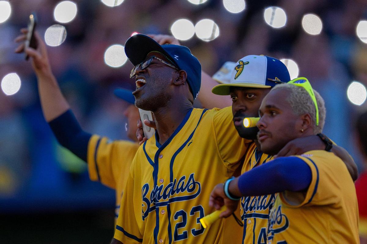 Savannah Bananas players sing during the seventh-inning stretch as fans wave their phone flashlights along to music during a Banana Ball game against the Firefighters at Kauffman Stadium on Friday, May 23, 2025, in Kansas City.