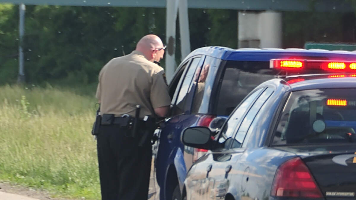 A police cruiser with the lights flashing has stopped a speeding car along the interstate highway and is issuing a ticket.