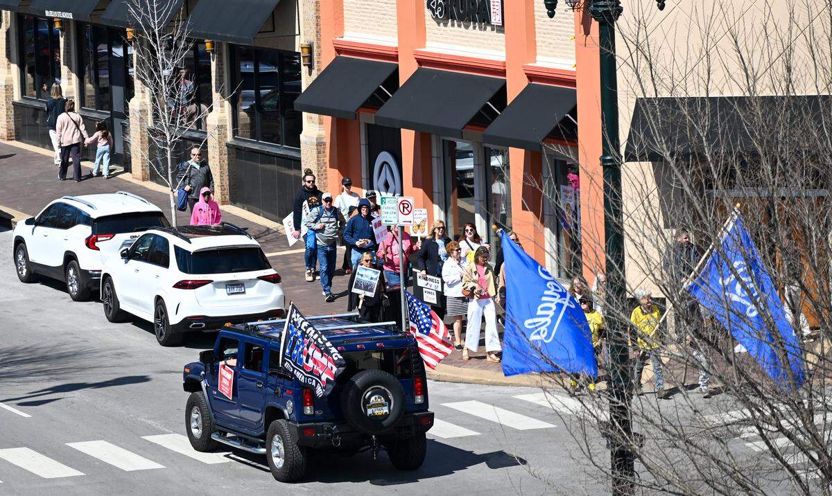 A car flying Trump flags drove by protesters gathered in Mill Creek Park near the Country Club Plaza on Saturday, March 28, 2026, for a No Kings protest against the Trump administration.