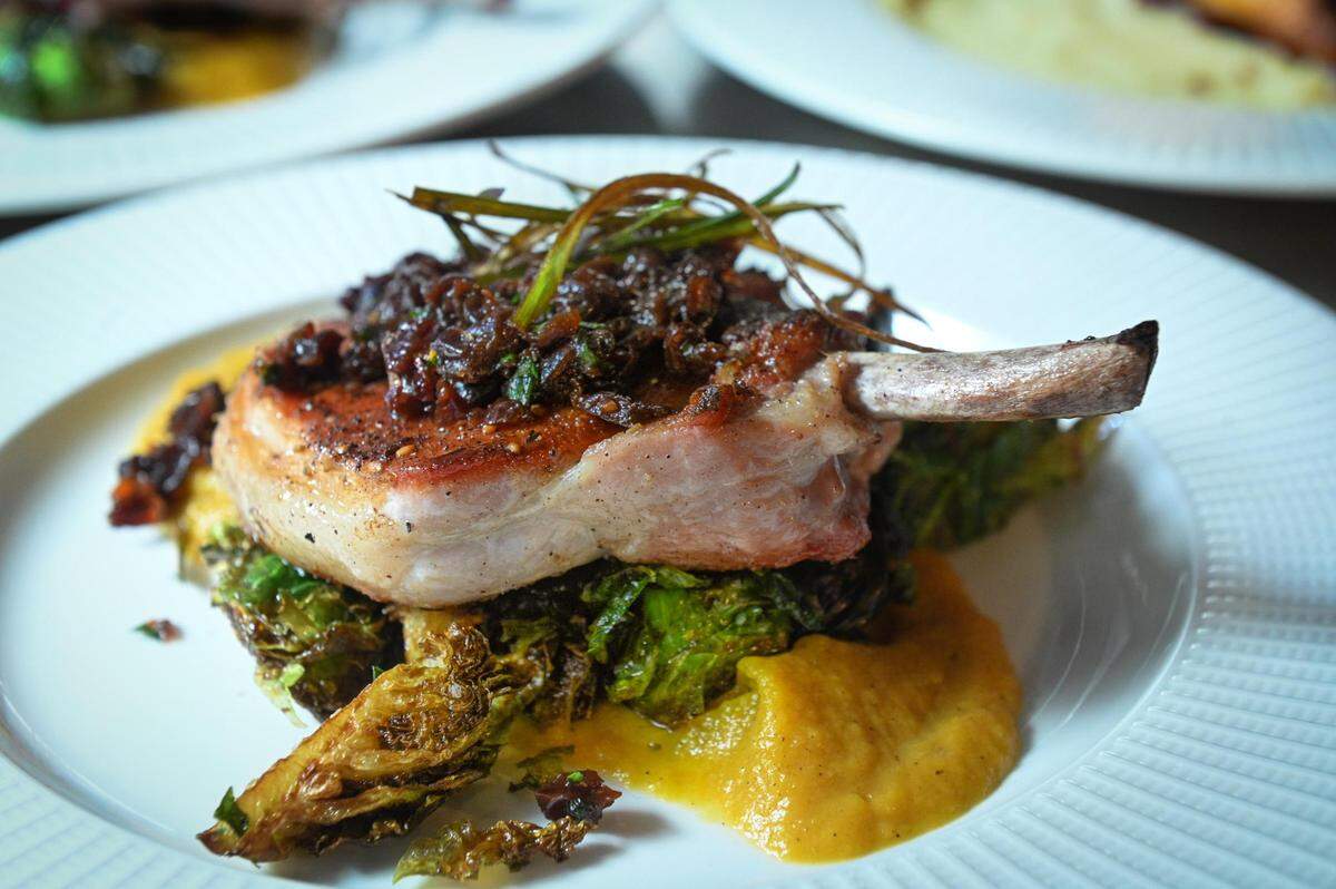 Za’atar seasoned pork chop with a squash puree, fried Brussels sprouts, agave cider butter, crispy green leek and dried cherry pico served during a soft opening Thursday at The Peacock.