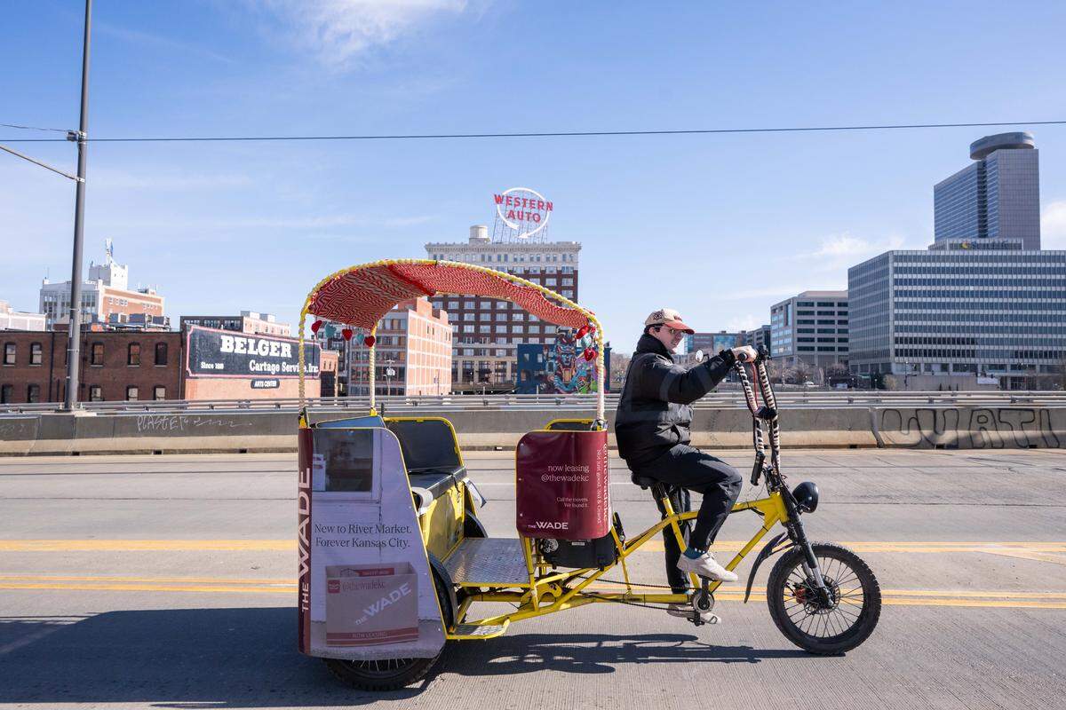 Mark Manning, co-owner of E-Z Pedicabs, rides past the Western Auto sign. The owners also operate the pedicabs and claim to serve as “ambassadors” of Kansas City to their riders, providing a different point of view than most modes of transportation.