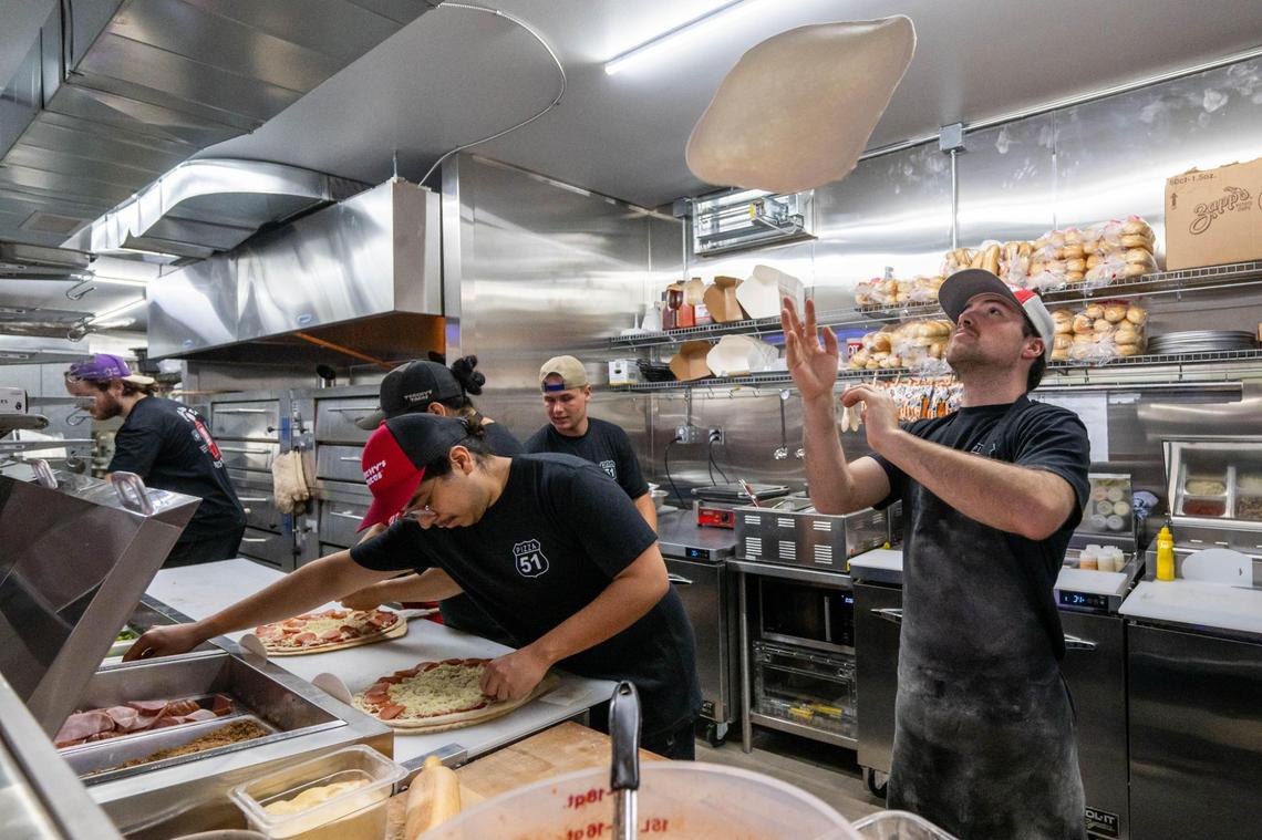 Josh Pryor, son of owners Jason and Shannon Pryor, flips pizza dough as the kitchen crew build pizzas during the grand opening of Pizza 51’s newest location in Olathe on Wednesday, June 25. The pizza place opened its newest location inside an old Phillips 66 service station.