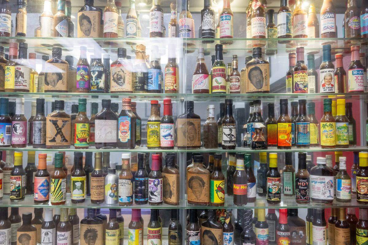 Hundreds of bottles of classic and current hot sauces in a glass case at the Spicin Foods warehouse on Southwest Boulevard, on October 2, 2025, in Kansas City. Spicin Foods produces one of the most famous hot sauces on the market, Da' Bomb Beyond Insanity, made famous by the YouTube show Hot Ones.