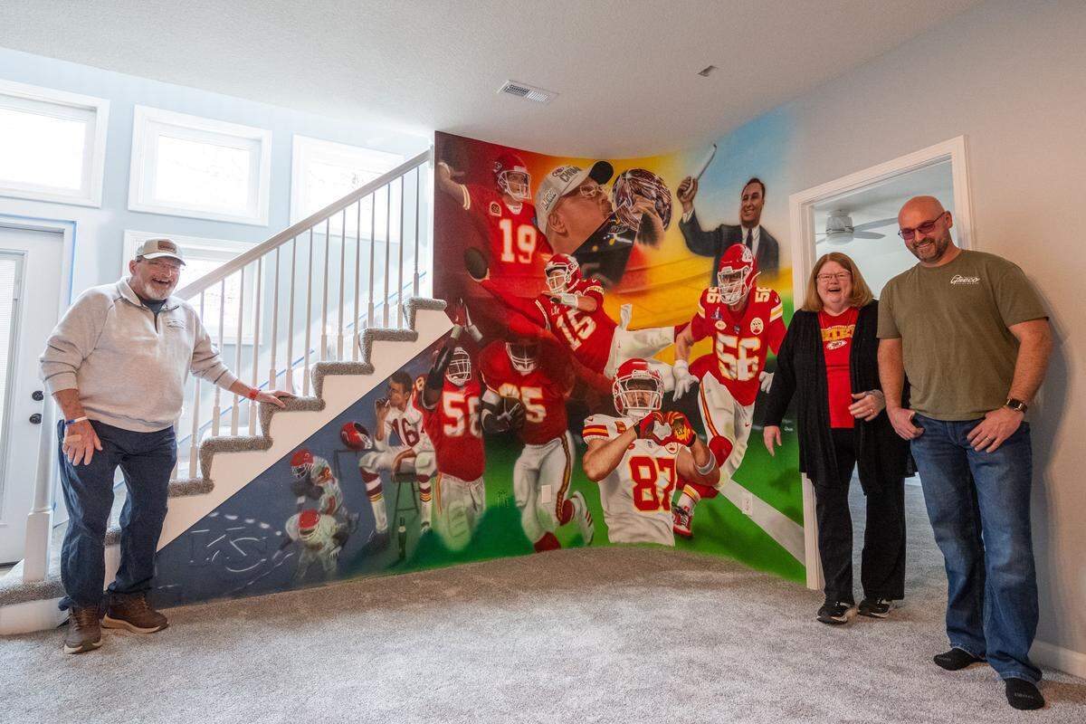 Ed and Mary Ellen Hughes and Kansas City artist Craig Greco stand next to a mural of past and present Chiefs players that Greco painted inside the Hughes' home in Liberty.