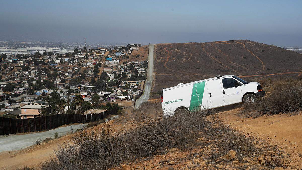 A U.S. Border Patrol van drives up the hill to pick up migrants apprehended trying to cross the U.S.-Mexico border illegally as the Mexican land looks on the left side of the border wall along a road Thursday.